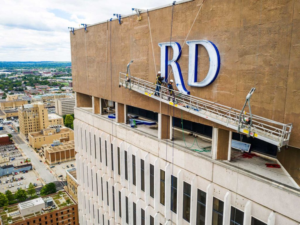 A large exterior sign being installed by Identiti atop a skyscraper by professionals on a large scaffolding.