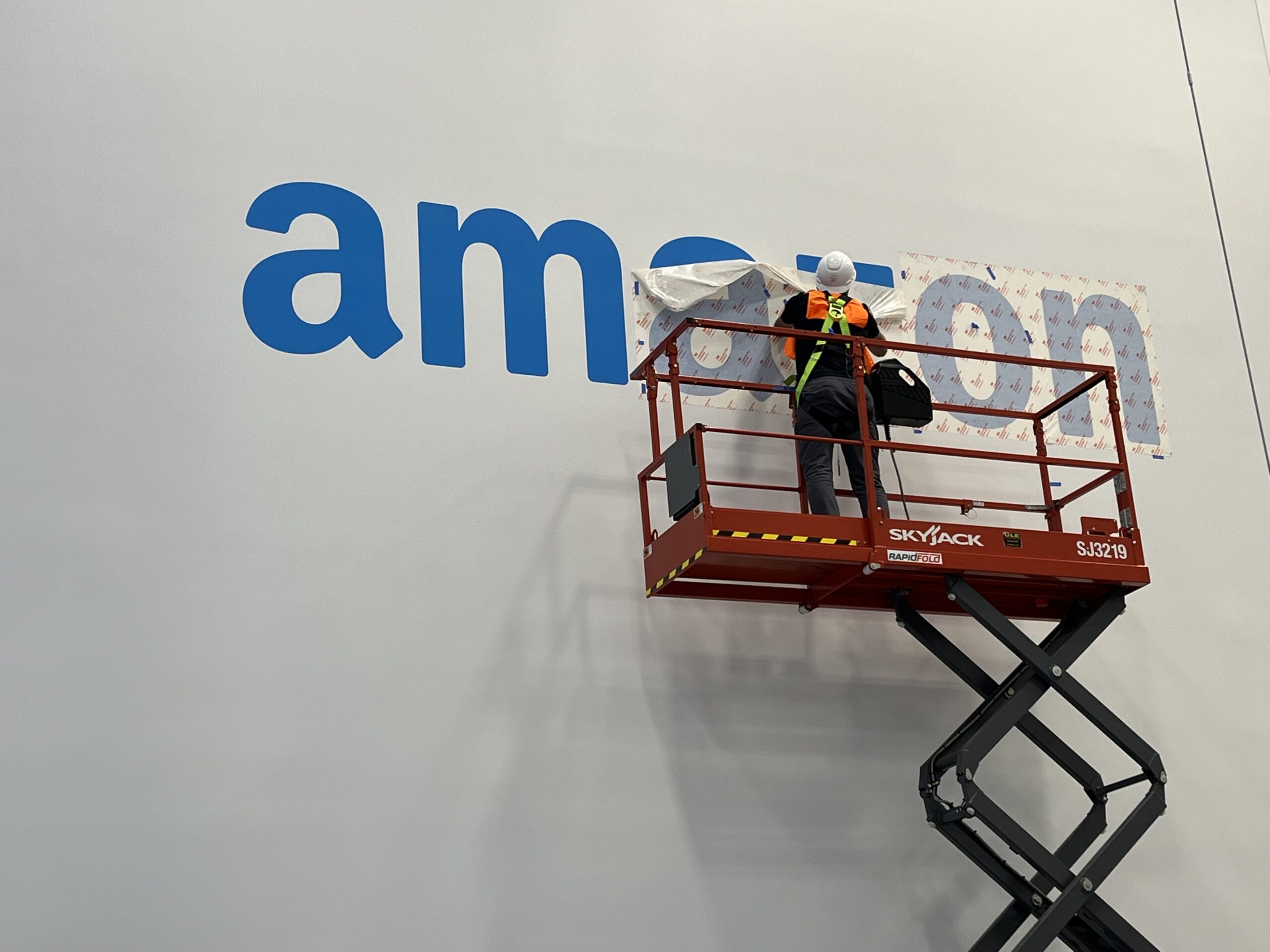 An installer applying wall graphics inside an Amazon fulfillment center.