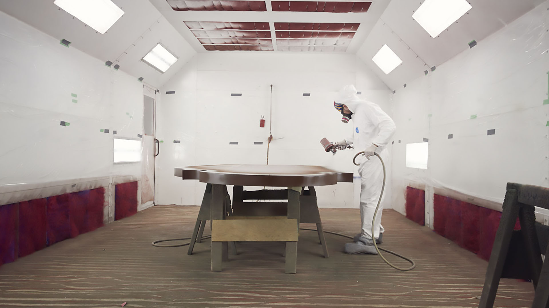 An employee applying a coat of paint with a sprayer in a paint booth.