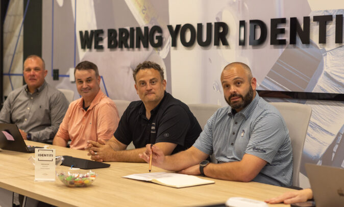 Four smiling Identiti team members sitting behind a conference table.