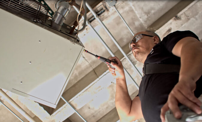 An Identiti maintenance professional working on an overhead HVAC system.