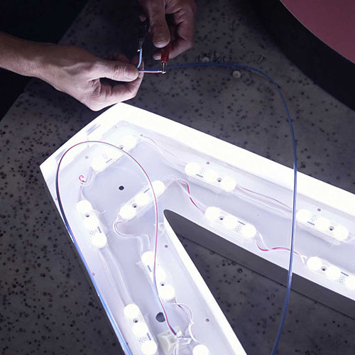 A hand works on illumination components for a channel letter.