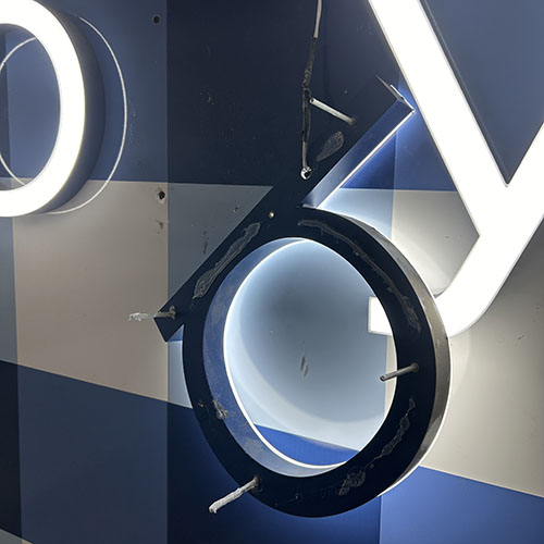 A damaged channel letter sign, hanging from the wall by an electrical wire.