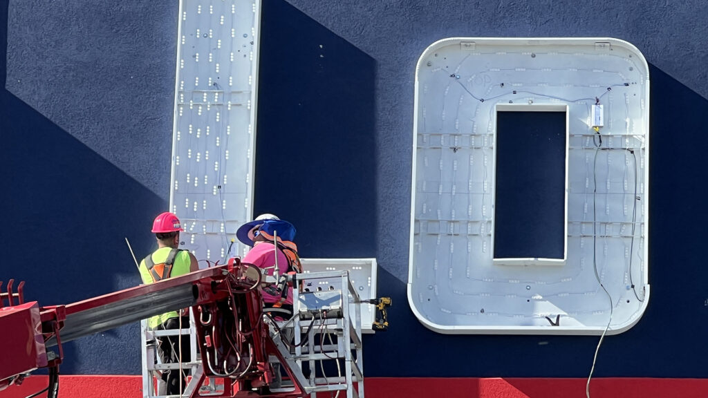 Two maintenance professionals working on a large illuminated exterior sign at a Lowe's location.