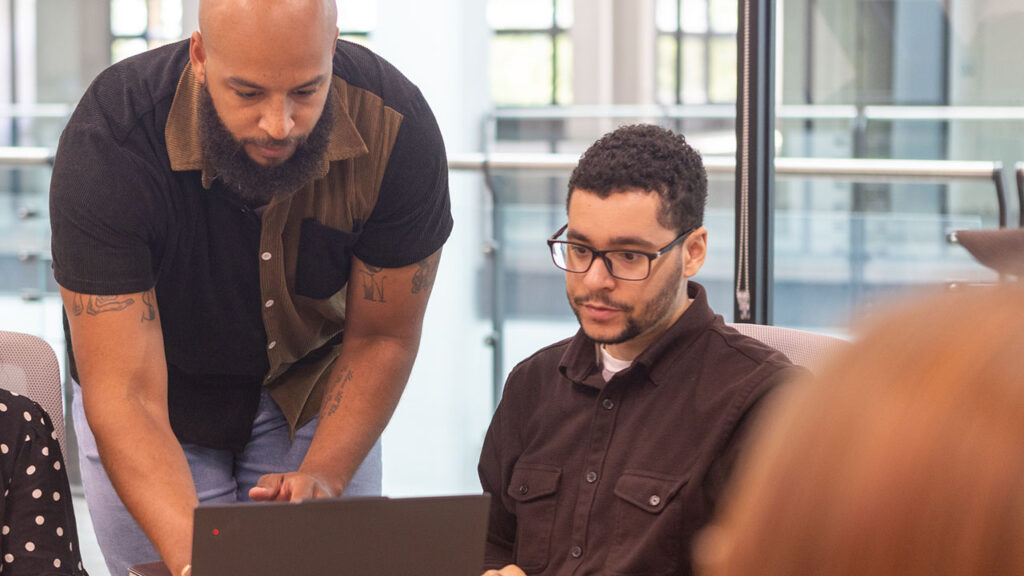 Two Identiti team members work together on a laptop computer.